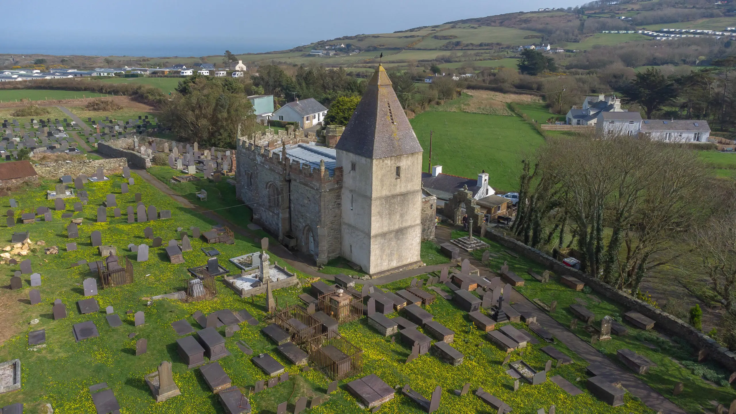 Eglwys a meindwr Llaneilian yn codi yn y blaendir gyda bae Dulas a Môr Iwerddon y tu ôl