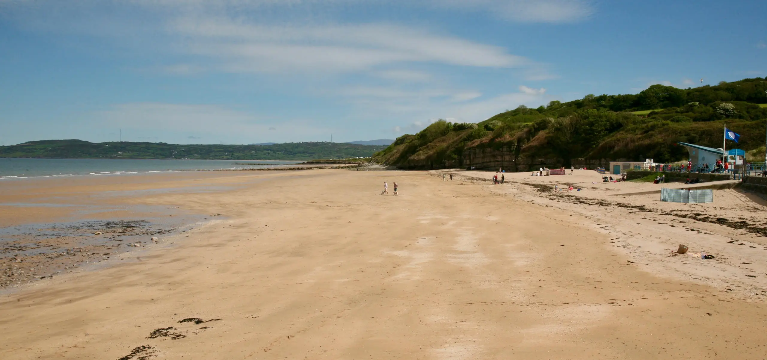 Traeth tywodlyd gyda'r môr yn treiglo a chymylau cumulus yn edrych o'r promenâd