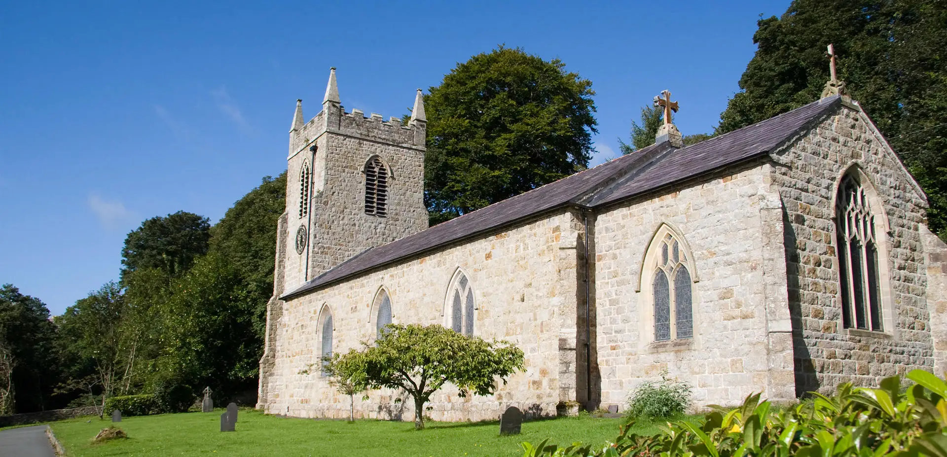 St Cyngars Church rising up with the entrance to the dingle just to the left and green trees.