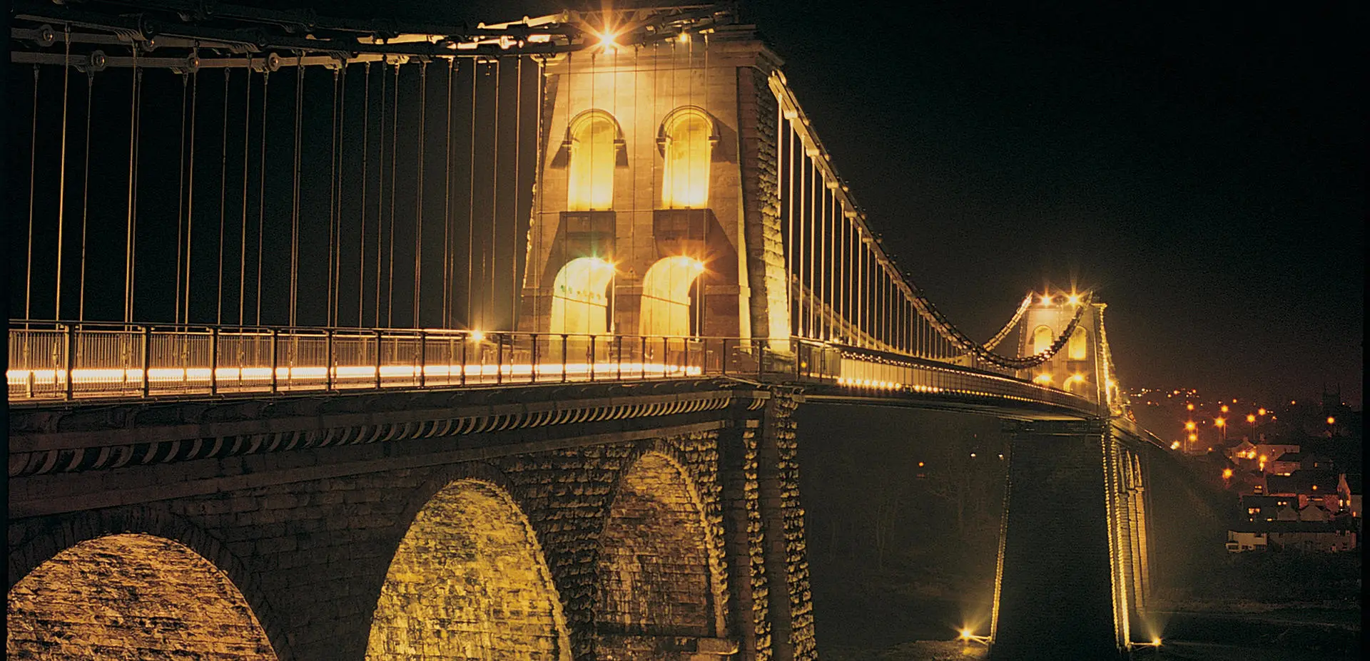 Pont Menai gyda'r nos gyda'r pileri wedi'u goleuo'n felyn disglair