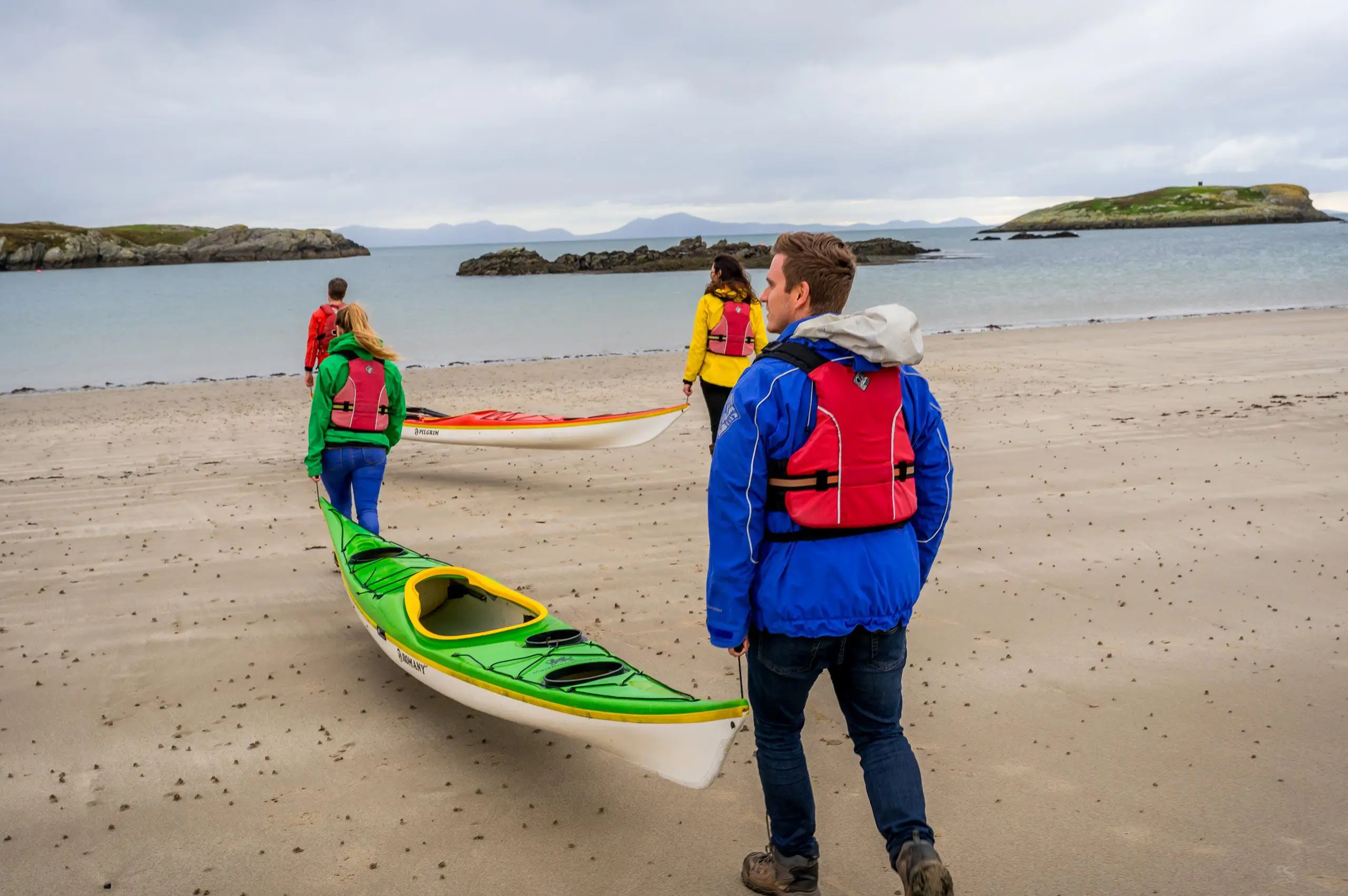 Pobl yn cerdded ar y traeth gyda kayak