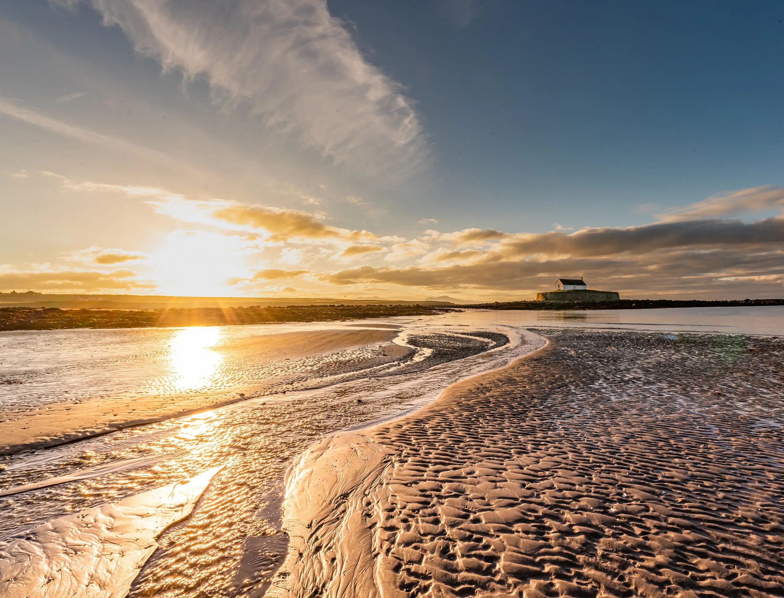 Eglwys Sant Cwyfan ar ynys fechan wedi'i hamgylchynu gan draeth gyda'r wawr