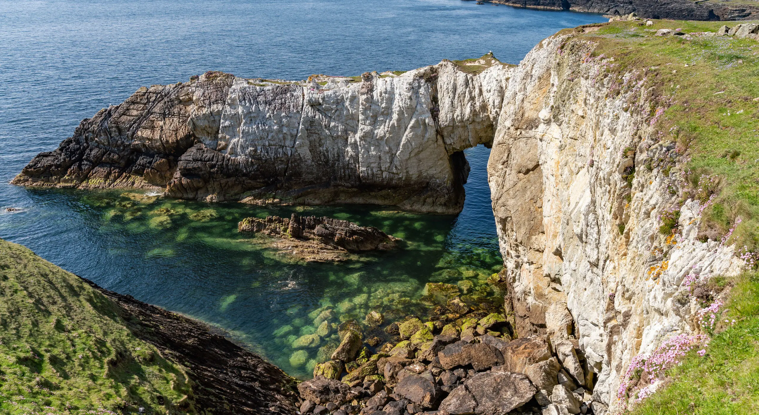 Bwa-gwyn-Rhoscolyn o'r clogwyn gyda'r môr glas yn y gwaelod