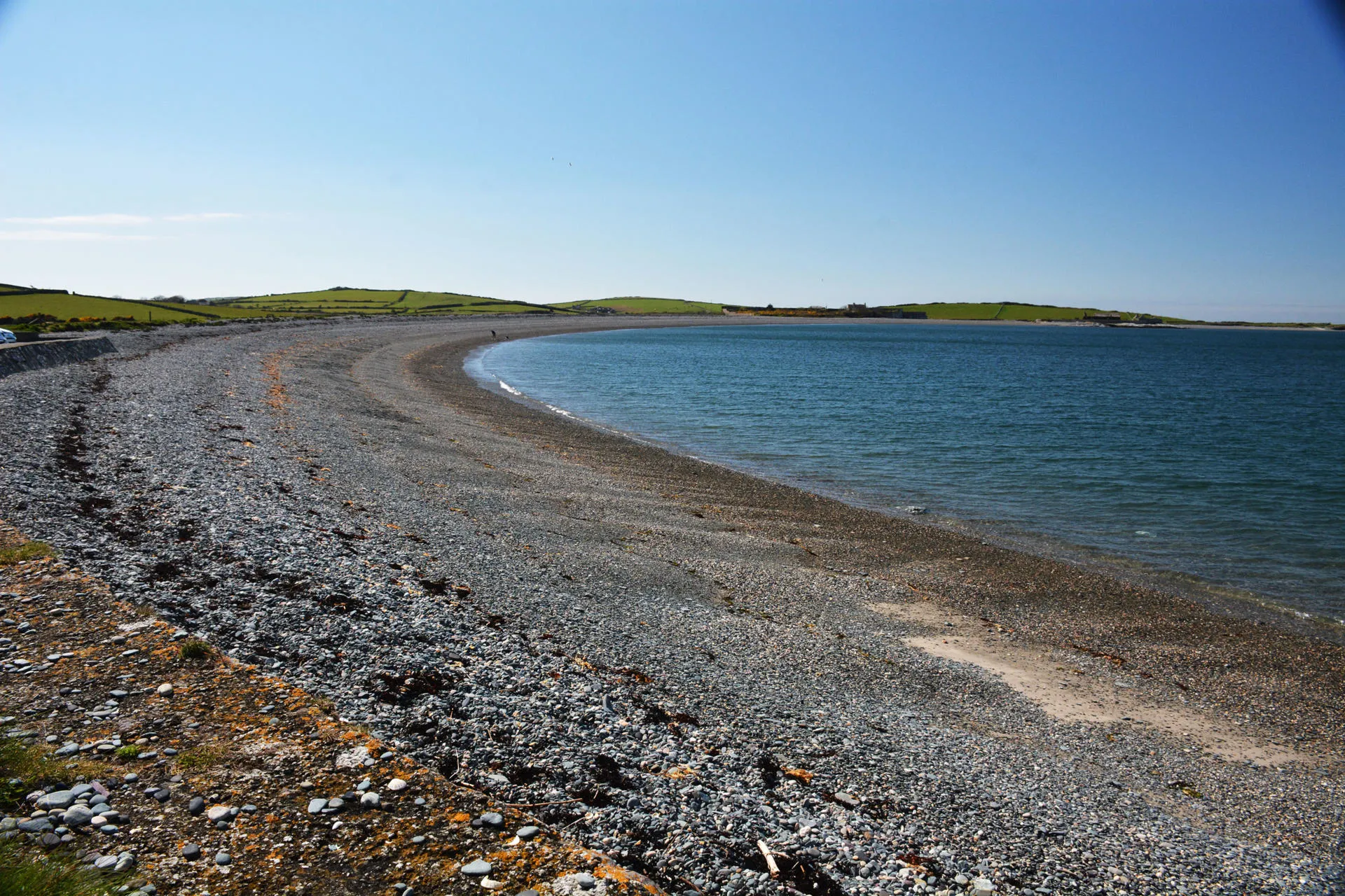 Traeth Cemlyn gyda'i flaendraeth creigiog graean a'i lagŵn glas i'r dde.