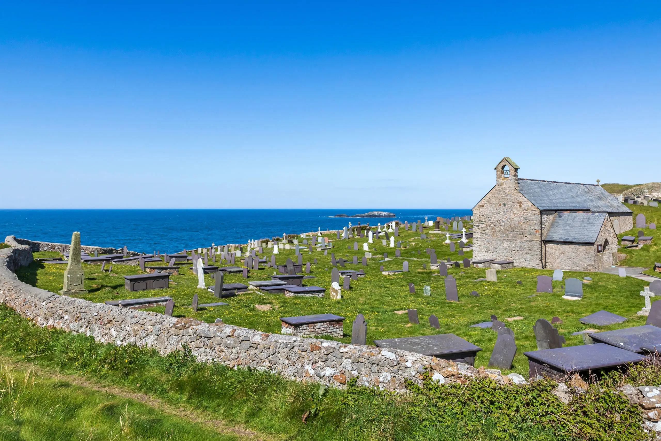 Eglwys Llanbadrig yn edrych allan i Fôr Iwerddon ar ddiwrnod o haf gyda awyr las a môr
